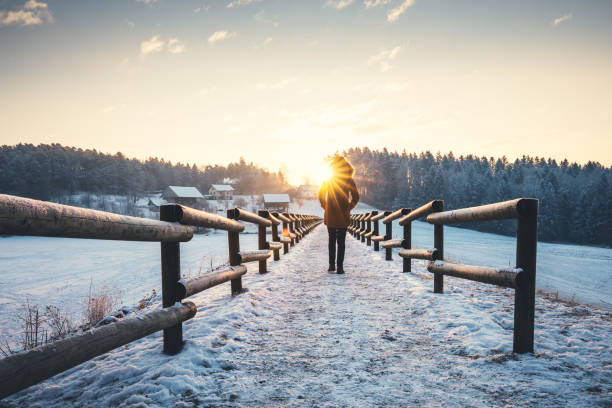 Woman walking at the frozen lake. Morning sun is peaking out from the trees.