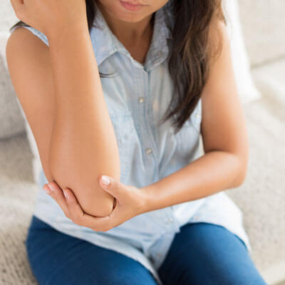 woman sitting down, holding her elbow in pain