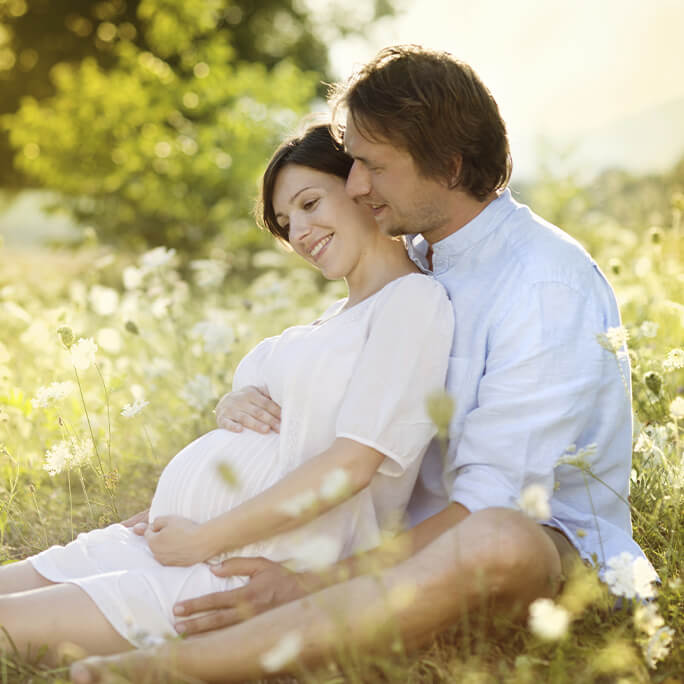 Husband and pregnant wife sitting in field