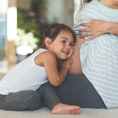 Girl with ear to mom's pregnant belly.