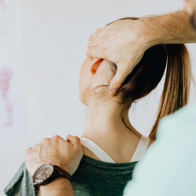 Back view of crop faceless bearded orthopedist in wristwatch checking up neck of anonymous lady while standing in front of wall with paper drawings representing body anatomy
