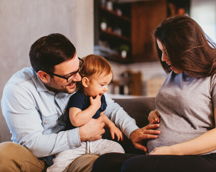 Man with baby on lap touching pregnant lady's belly