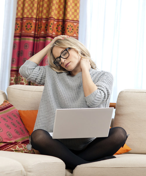woman sitting on couch with neck pain and lap top on lap