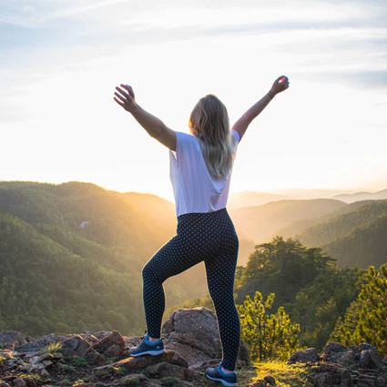 woman standing against the sun arms raised