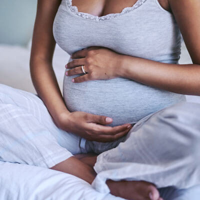 pregnant mom in pajamas sitting on a bed