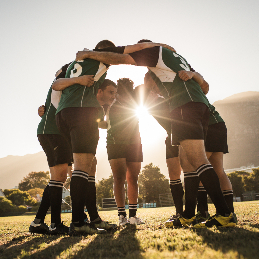 Rugby players standing in a circle with their hands on shoulders. Rugby team in huddle after the match