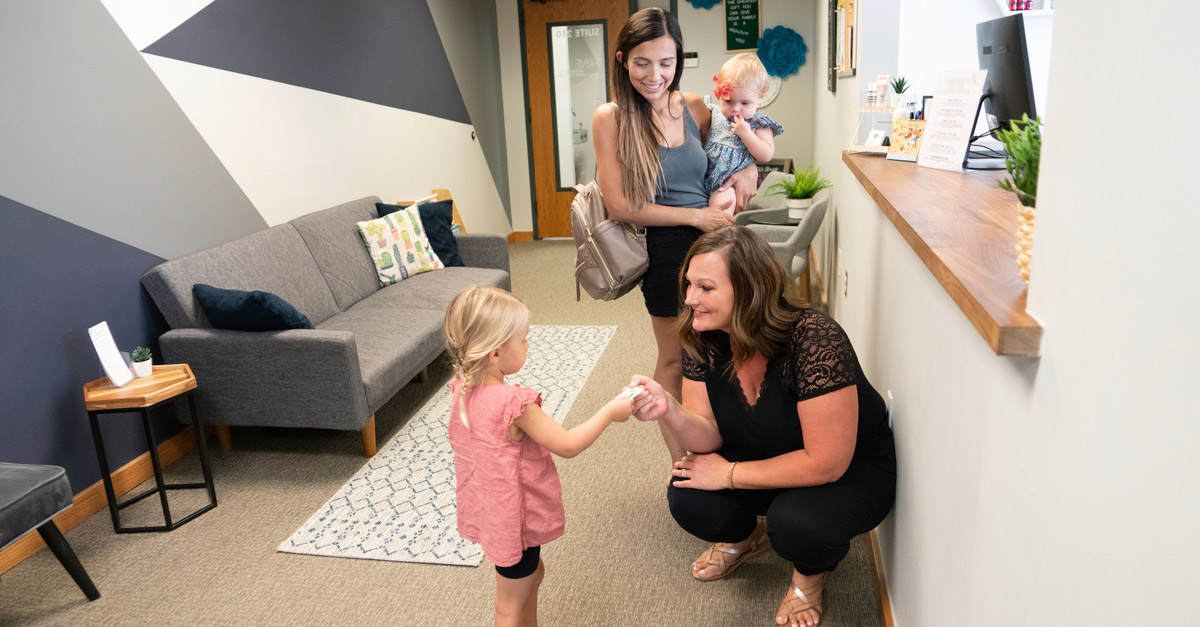 receptionist greeting little girl with mom and baby