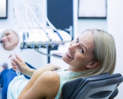 Smiling lady holding mirror sitting on dental chair