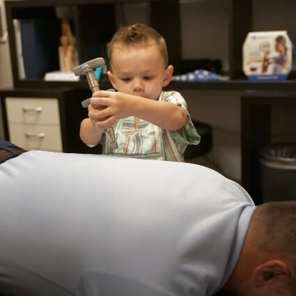 boy using chiropractic tool on chiropractor