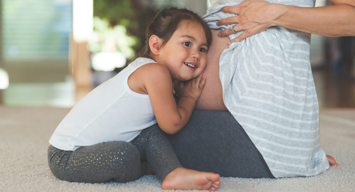 Little girl with ear on pregnant mom's stomach