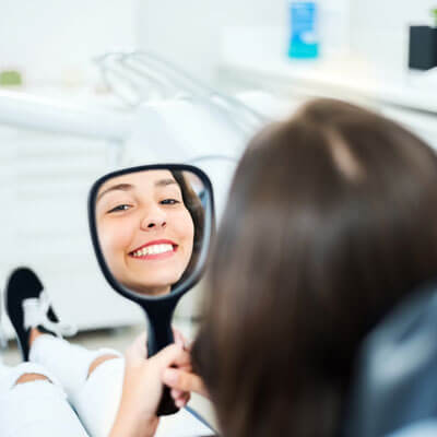 smiling woman looking at her teeth in a hand mirror