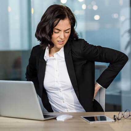 woman at desk holding lower back in pain