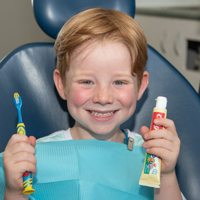 cute little boy smiling holding toothbrush and toothpaste on dental chair