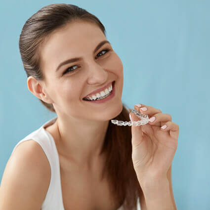 woman-smiling-holding-dental-aligner-blue-background-sq
