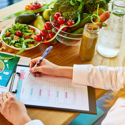 person-writing-on-paper-surrounded-by-healthy-vegetables-and-smoothie-sq