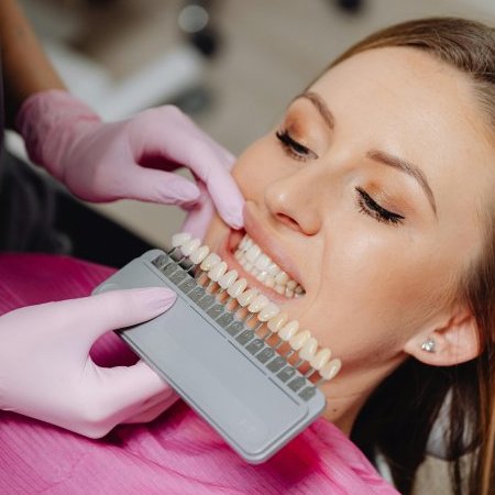 A woman undergoing a dental check-up with a shade guide to match teeth color in a dental clinic.