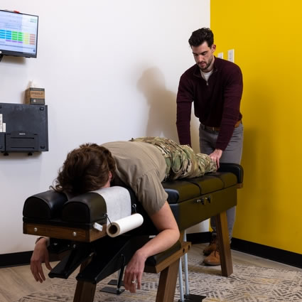 Dr. Dylan adjusting a woman who is wearing military fatigues