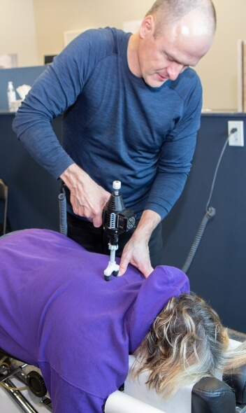 Dr. Tim using a chiropractic adjustment tool on a patient's back