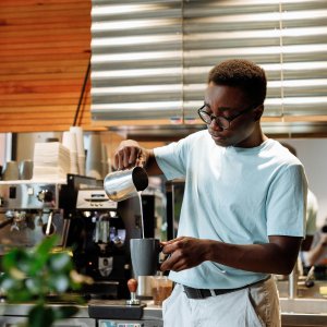 Barista pours steamed milk into coffee mug at a trendy cafe.