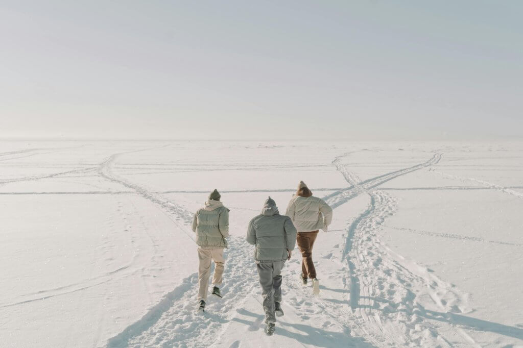 Three people running across a vast snowy field in winter attire.
