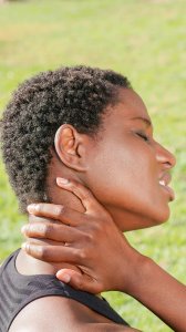 A woman outdoors holding her neck in discomfort, indicating pain or injury.