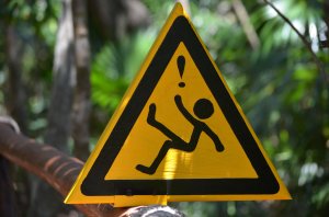 Yellow triangular warning sign indicating slippery surface in lush forest setting.