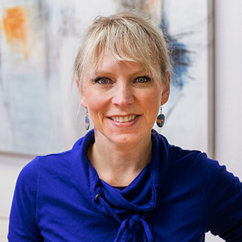 Marastella Mercer, LMT, at Spine Body Collective in Centennial, CO, standing in front of a plant and abstract artwork.