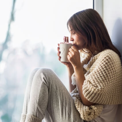 woman drinking hot drink sitting near a window