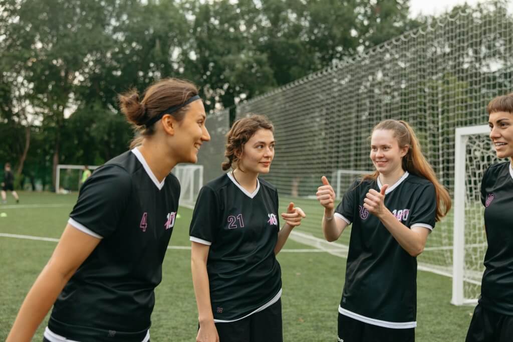 Group of female soccer players in black uniforms bonding outdoors, fostering teamwork.