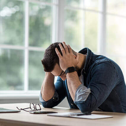 man at computer holding head in both hands