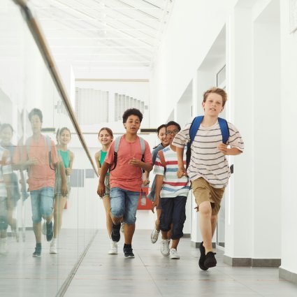 Group of diverse kids joyfully running in a bright school hallway.