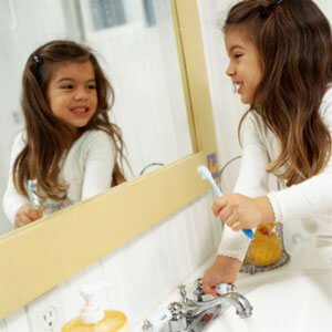 Little girl brushing teeth in mirror