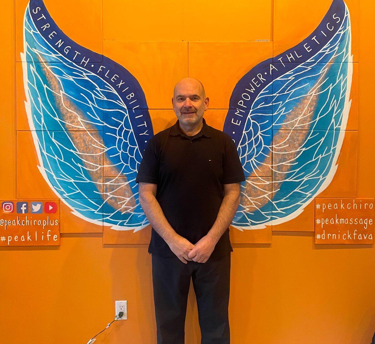 Dr. Nick Fava standing in front of the Peak Chiro Plus wall mural
