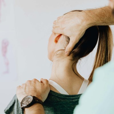 Back view of crop faceless bearded orthopedist in wristwatch checking up neck of anonymous lady while standing in front of wall with paper drawings representing body anatomy