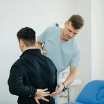 Chiropractor assisting a patient with back pain in a clinic setting.