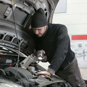 A mechanic closely inspects a car engine in a garage using a flashlight, ensuring proper maintenance.