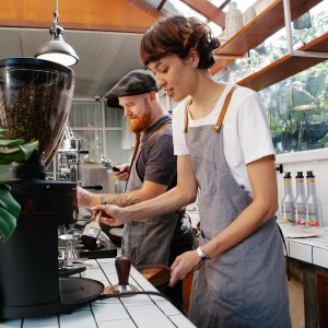 Coffee shop employees grinding fresh coffee beans and preparing espresso.