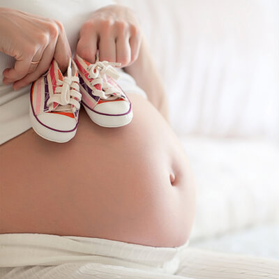 pregnant person holding baby shoes