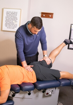 Chiropractor adjusting a male patient wearing a orange shirt
