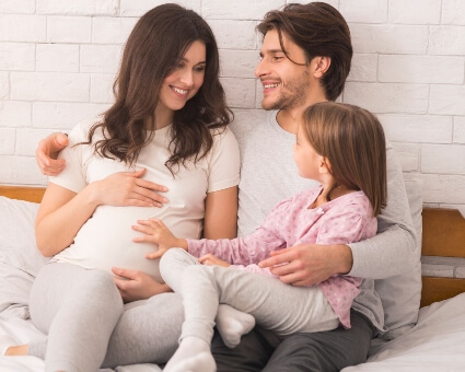 Pregnant lady sitting with family on bed