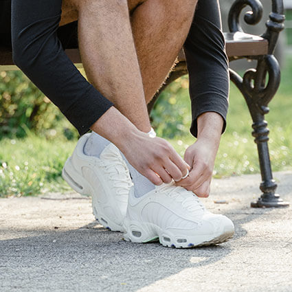 person tying their shoes while sitting on a bench