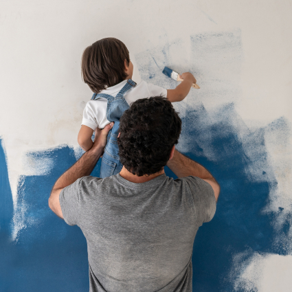 Man holding a child painting a wall