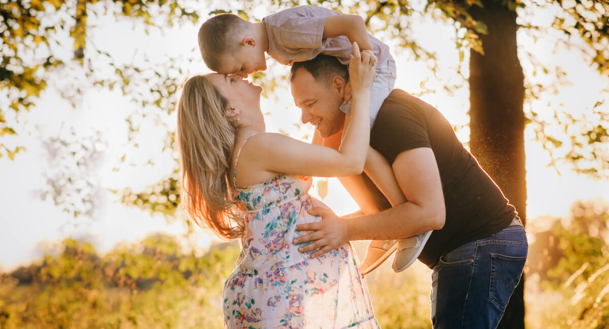 Smiling pregnant mom out in nature with husband and young son