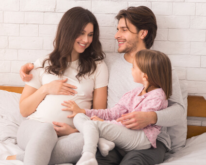 Pregnant mom on bed with husband and young daughter