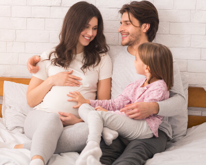 Pregnant mom sitting on bed with husband and young child