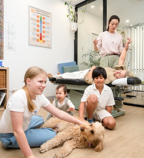 Lindfield chiropractor Dr Jane adjusting practice members while kids play with our office dog