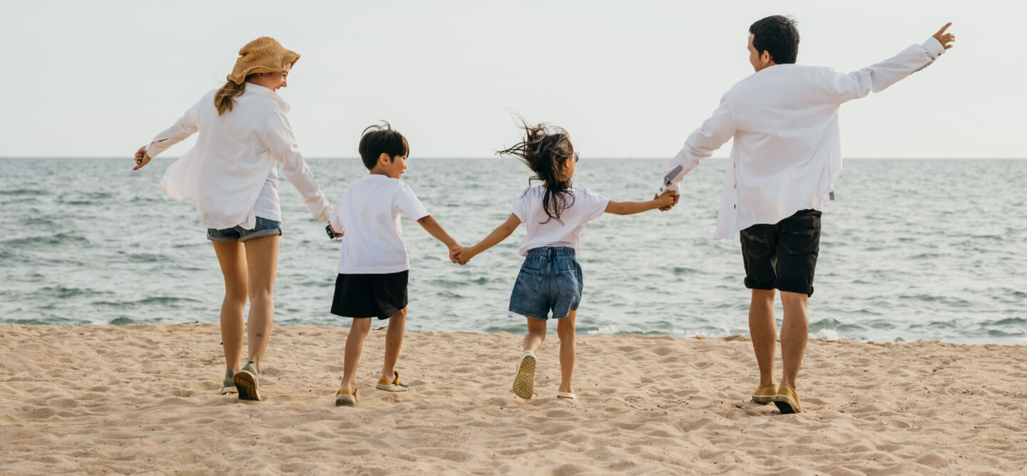 family of 4 walking on the beach holding hands