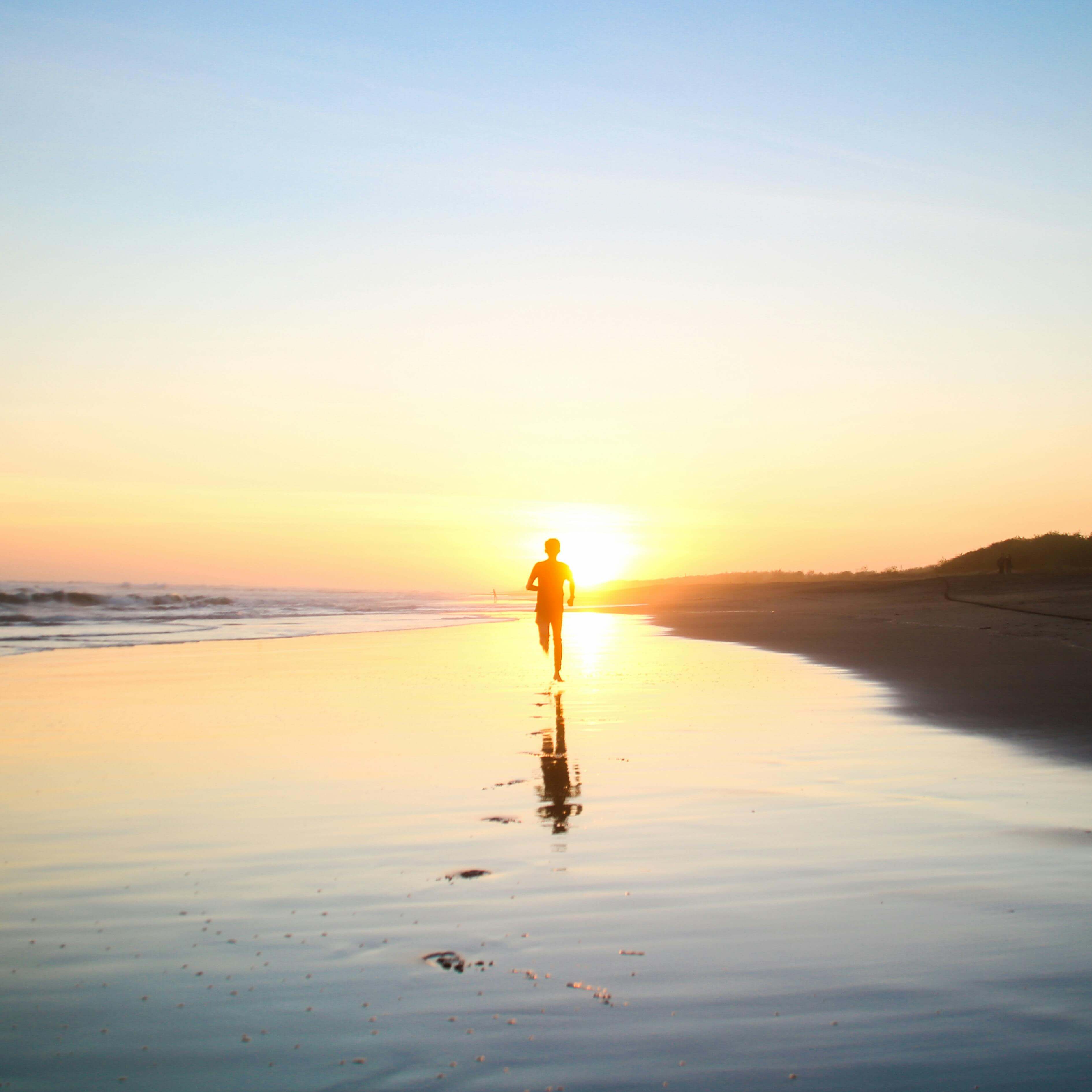 A lone silhouette of a person running along a serene beach at sunset, reflecting in the wet sand.