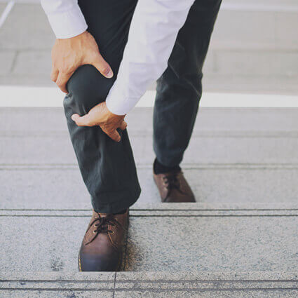 man walking upstairs holding leg in pain