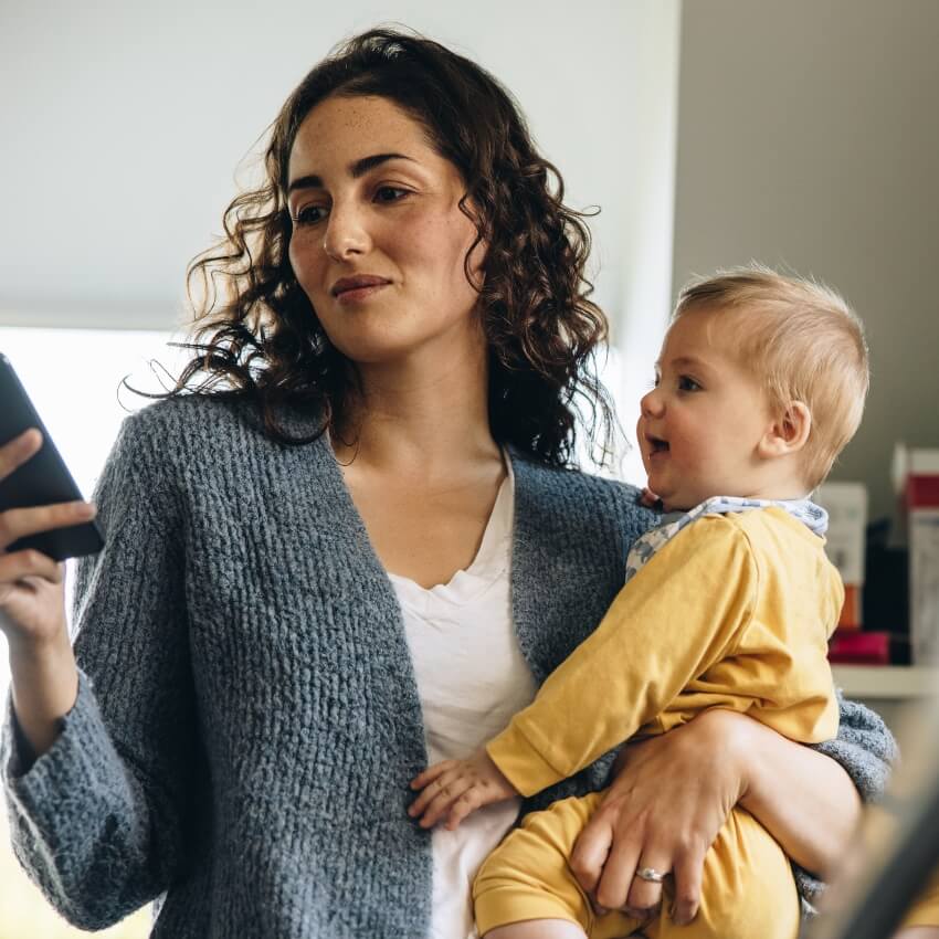 Woman holding her baby and texting on her phone